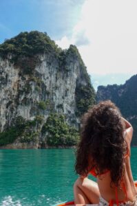 Solo female traveler looking out at the limestone cliffs while sailing through khao sok national park in thailand