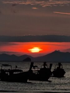 red sunset and long tail boats from railay beach, krabi, thailand