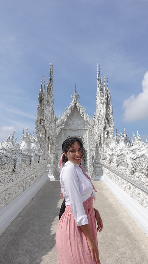 solo female traveler standing in front of white temple while visiting chiang rai thialand