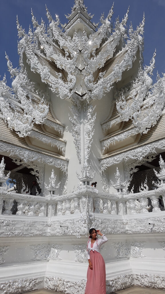 solo female traveler standing near white temple in chiang rai thailand