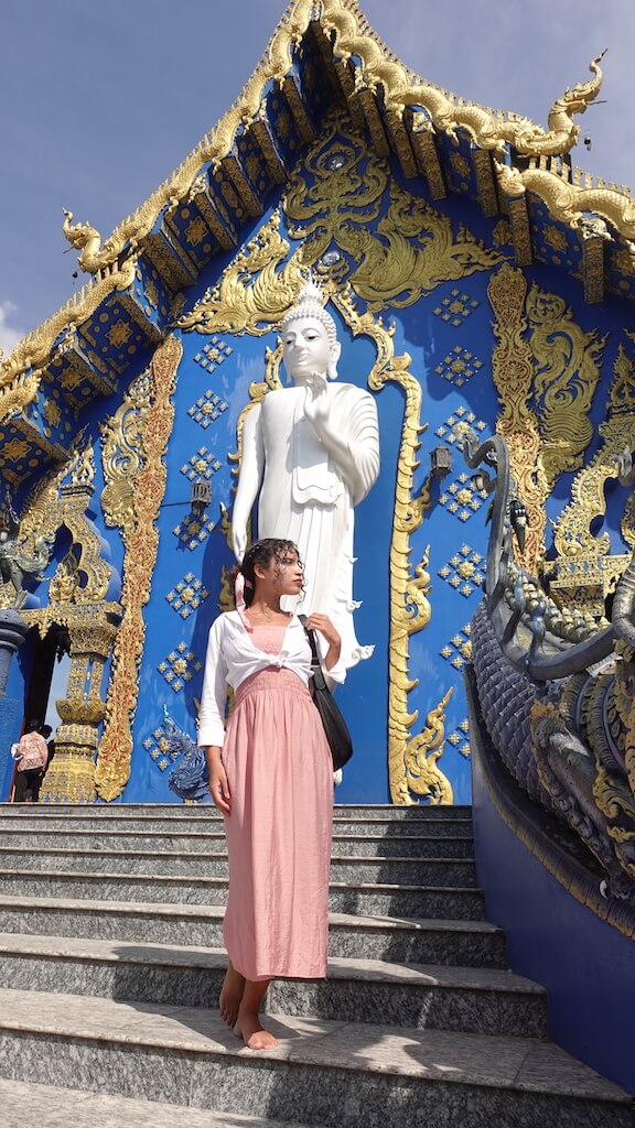 Solo female traveler standing on the steps of the blue temple in chiang rai thailand