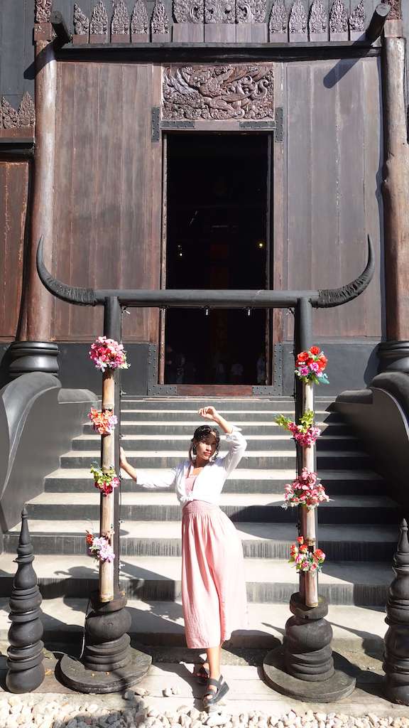 Solo female traveler standing in front of steps of the black temple in chiang mai thailand