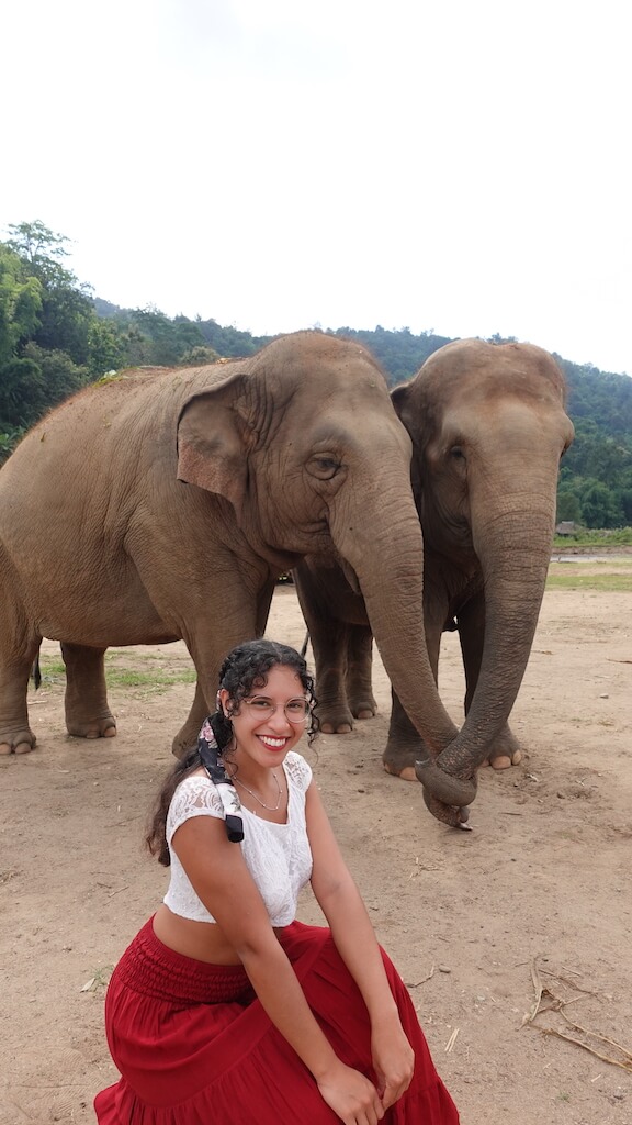 Solo female traveler posing next to two elephants holding each others trunks