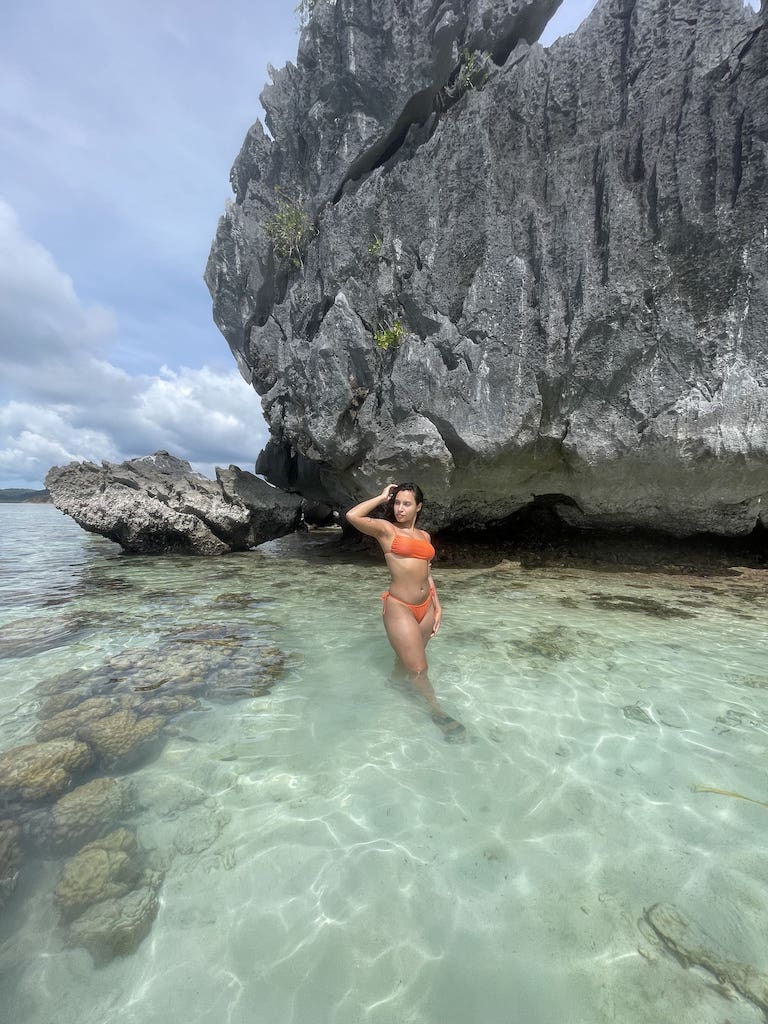 Solo female traveler standing in crystal clear water while visiting Coron, Philippines