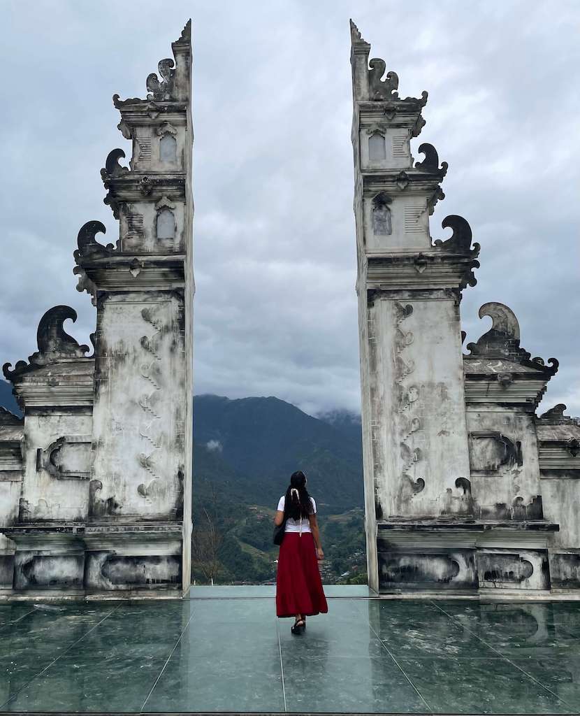 Solo female traveler between two towers in Moana Sapa Vietnam while wearing a white skirt and red skirt with a black hobo purse and black sandals