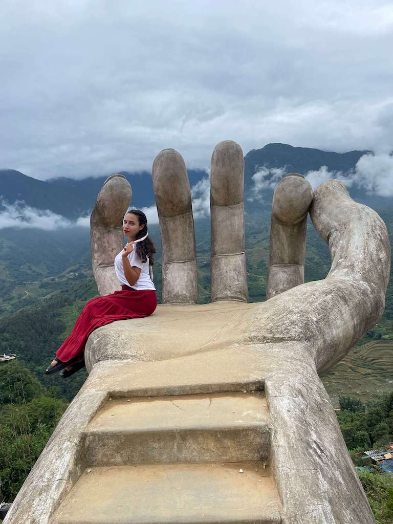 Solo female traveler sitting on floating hand in Moana Sapa Vietnam while wearing a white t shirt and red skirt with pink ribbon in her hair and black sandals