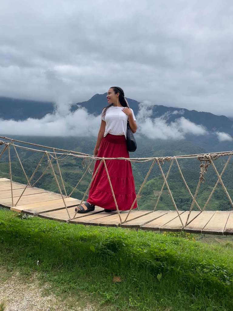 Solo female traveler on floating bridge in Moana Sapa Vietnam among white floating clouds atop the mountain